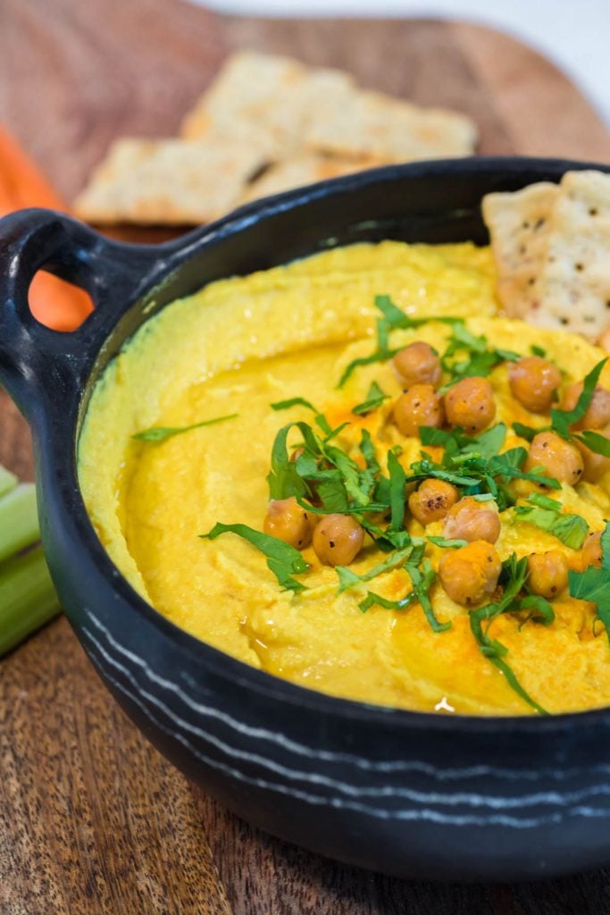 golden hummus topped with chickpeas and parsley and served in a black bowl