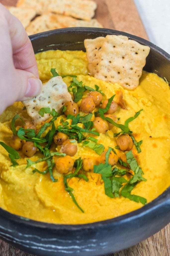 homemade turmeric hummus being scooped up with a plain cracker