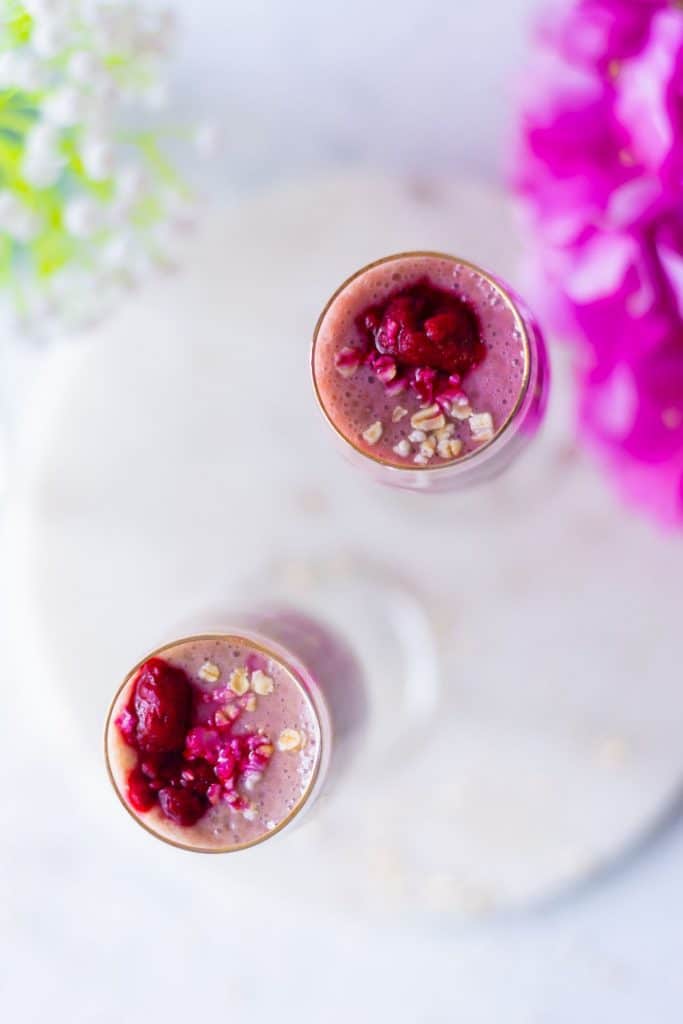 Overhead shot of a pink smoothie with some crushed raspberries and oats on top