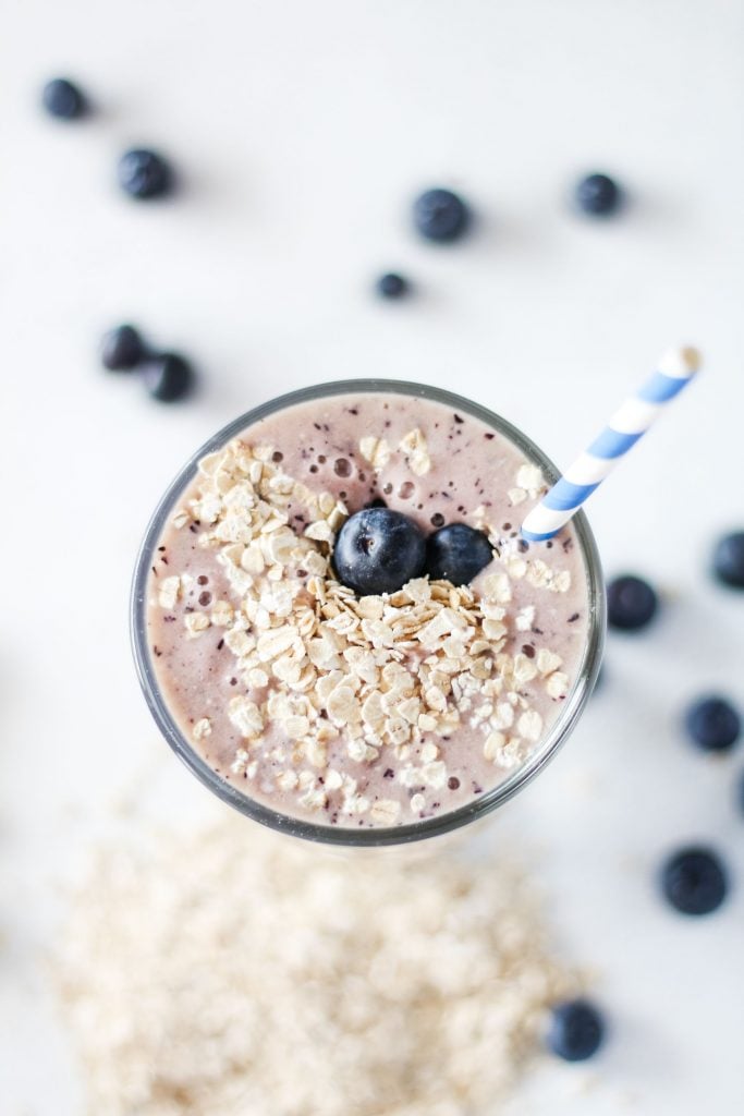 overhead shot of a blueberry smoothie served in a tall glass and topped with fresh blueberries and oats