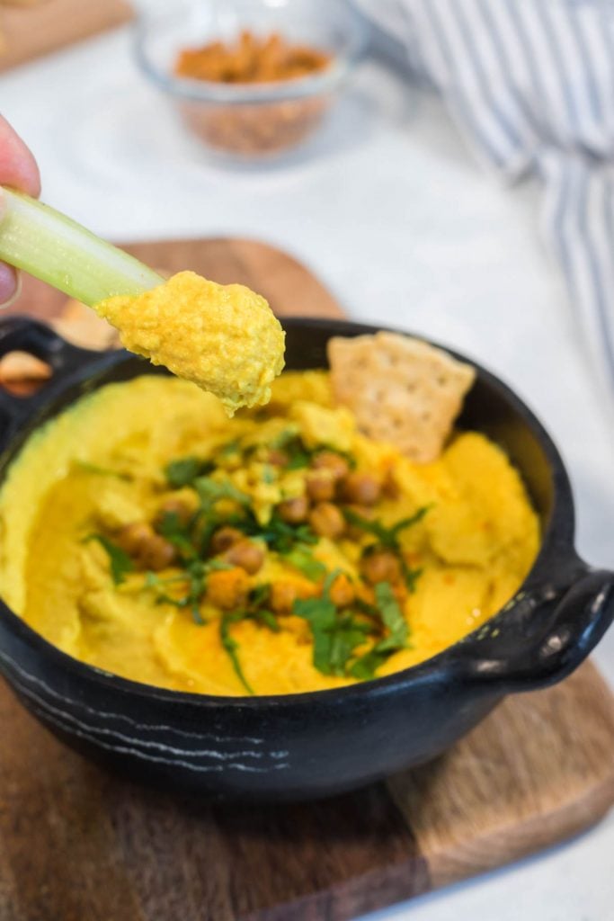 stick of celery scooping up some homemade turmeric hummus from a black bowl