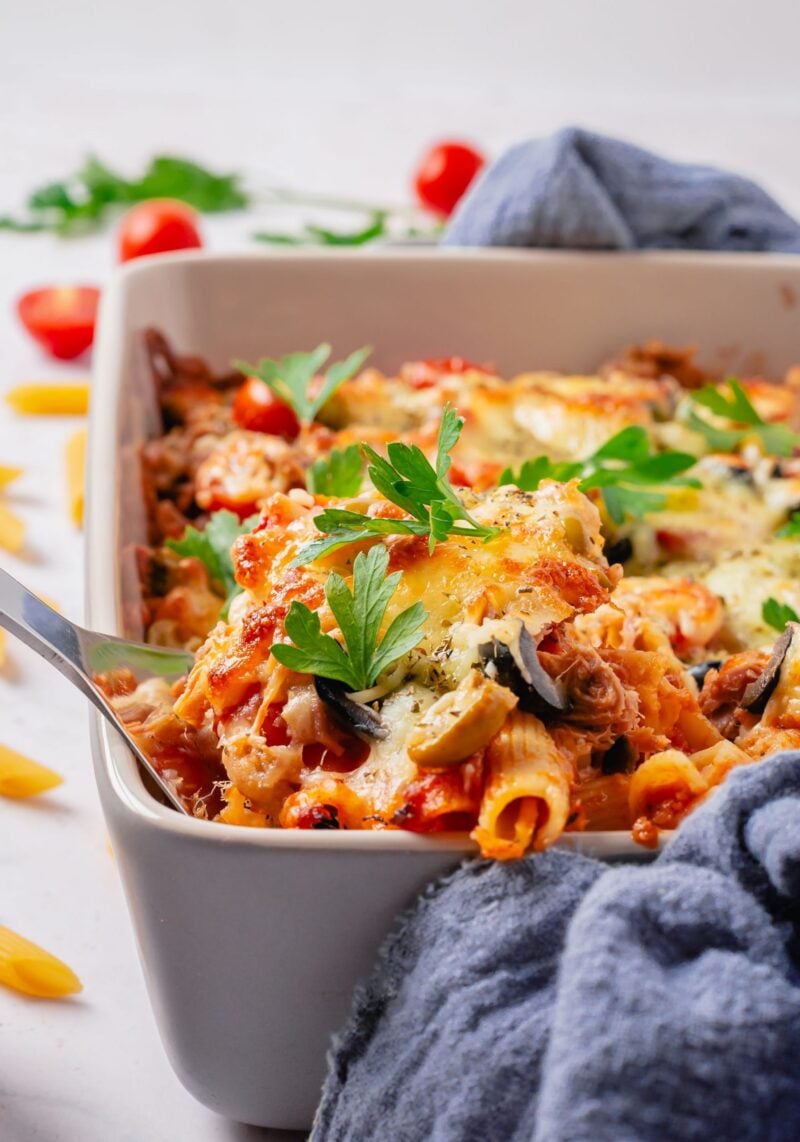 Tuna casserole in a white casserole dish with some dry pasta and cherry tomatoes in the background