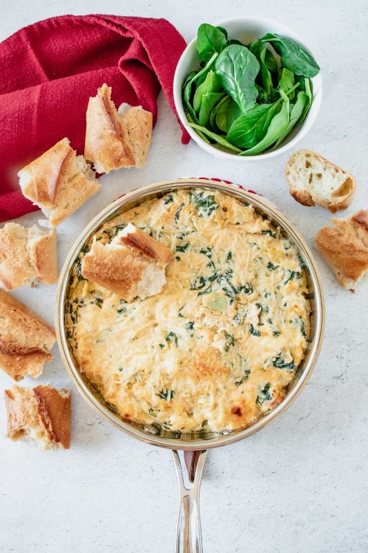 overhead shot of a creamy dip in a saucepan surrounded by crusty bread