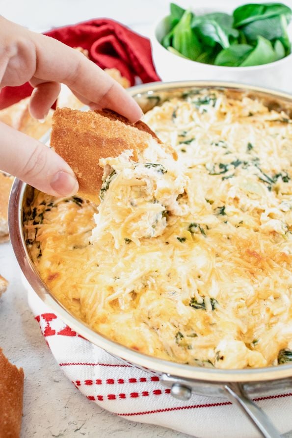 Crunchy bread being dipped into a cheesy artichoke dip