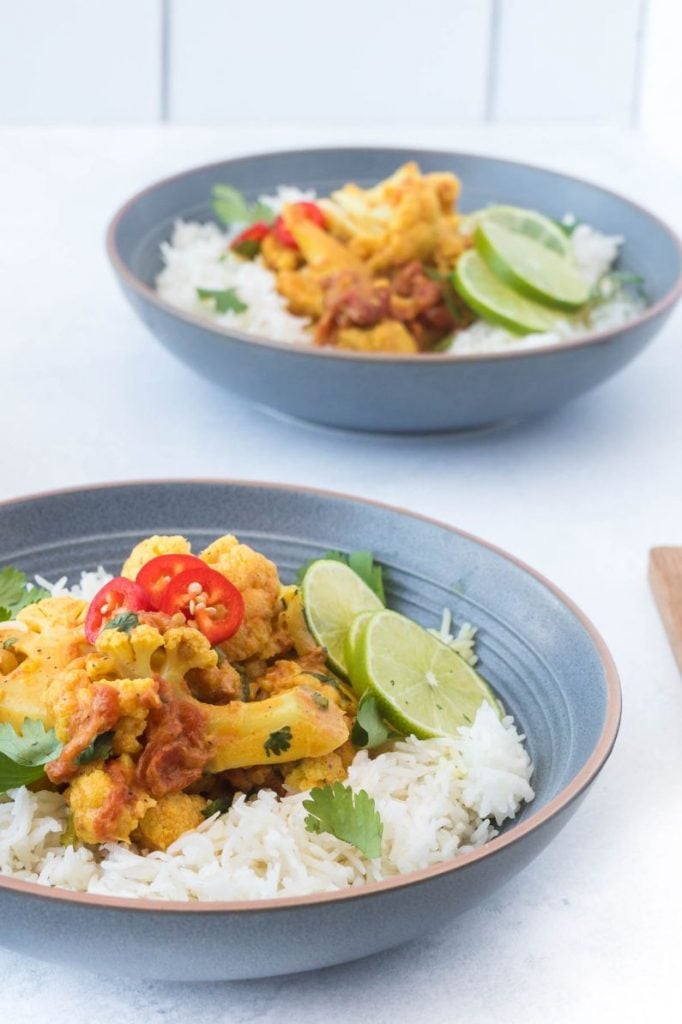 two blue bowls holding curry and rice, topped with lime, cilantro and chillies