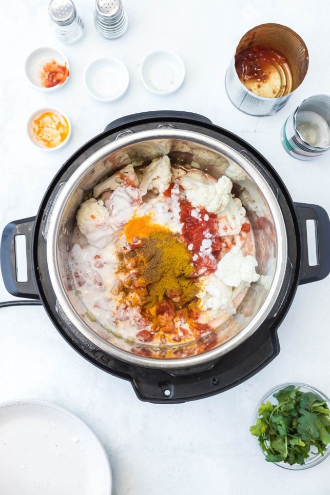 Cauliflower, tomatoes, herbs and spices being added to an instant pot
