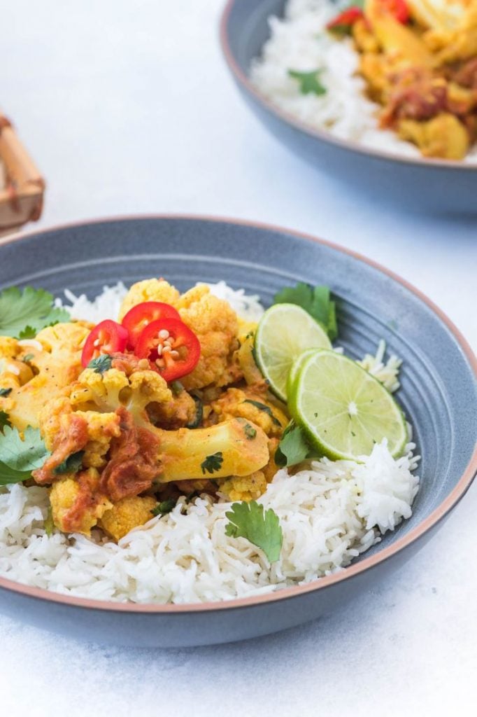 Curried cauliflower serving over a bed of rice and topped with chillies, cilantro and lime