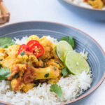 cauliflower curry served on a bed of steamed rice and topped with cilantro, lime slices and red chillies