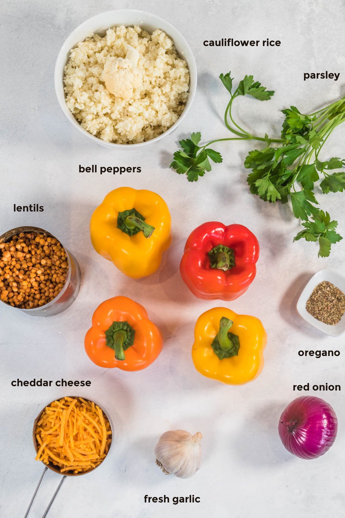 Overhead ingredient shot including multicolored bell peppers, red onion, cauliflower rice, lentils, cheese, parsley, oregano, and garlic.