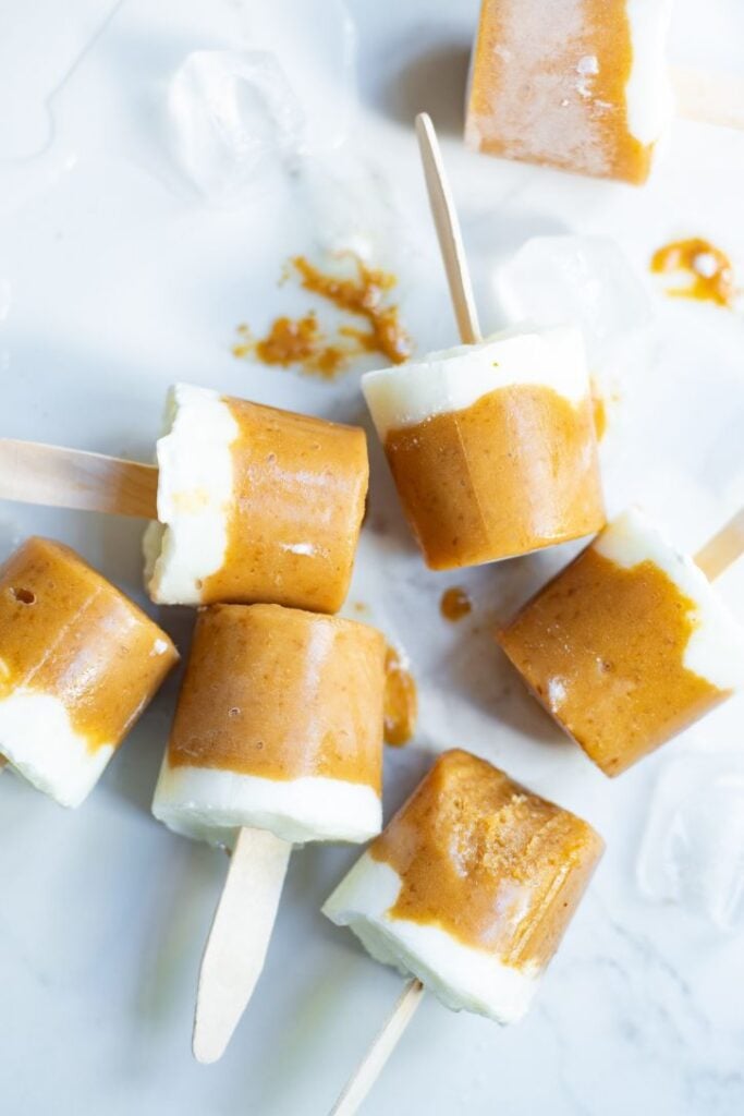 overhead shot of orange and white popsicles on wooden popsicle sticks with ice cubes in the background