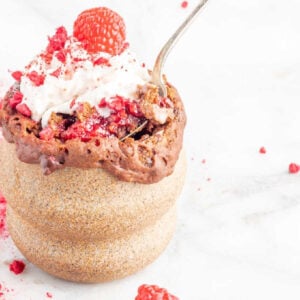 Silver spoon removing a spoonful of raspberry and chocolate cake from a beige mug