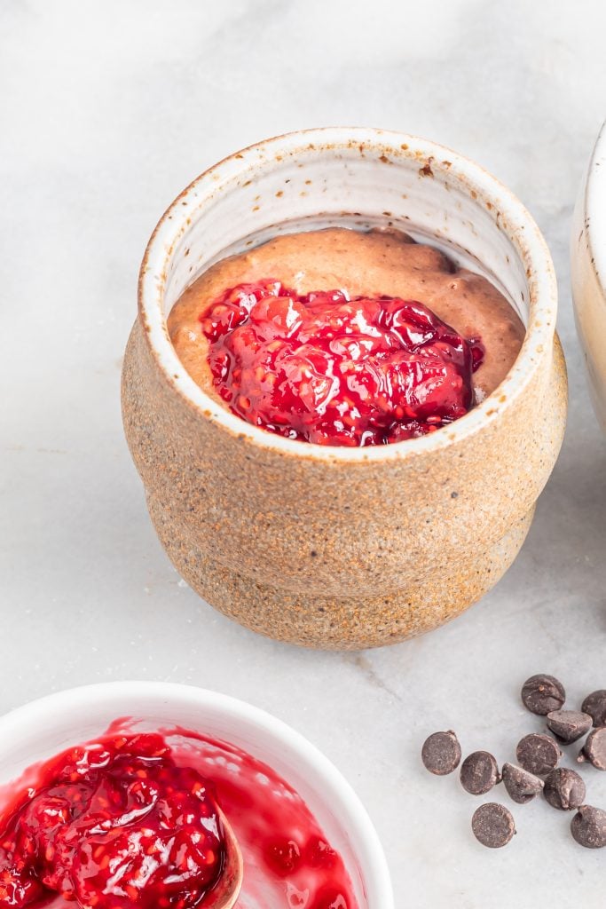 A dollop of raspberry jam added on top of chocolate cake batter in a mug