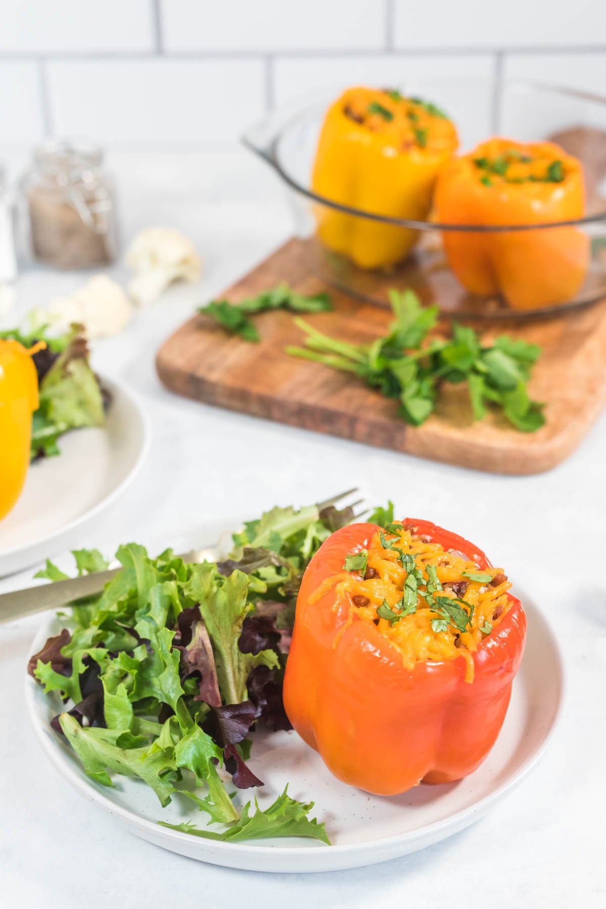 a bell pepper stuffed with spiced cauliflower rice and topped with cheese served on a white plate with a simple side salad