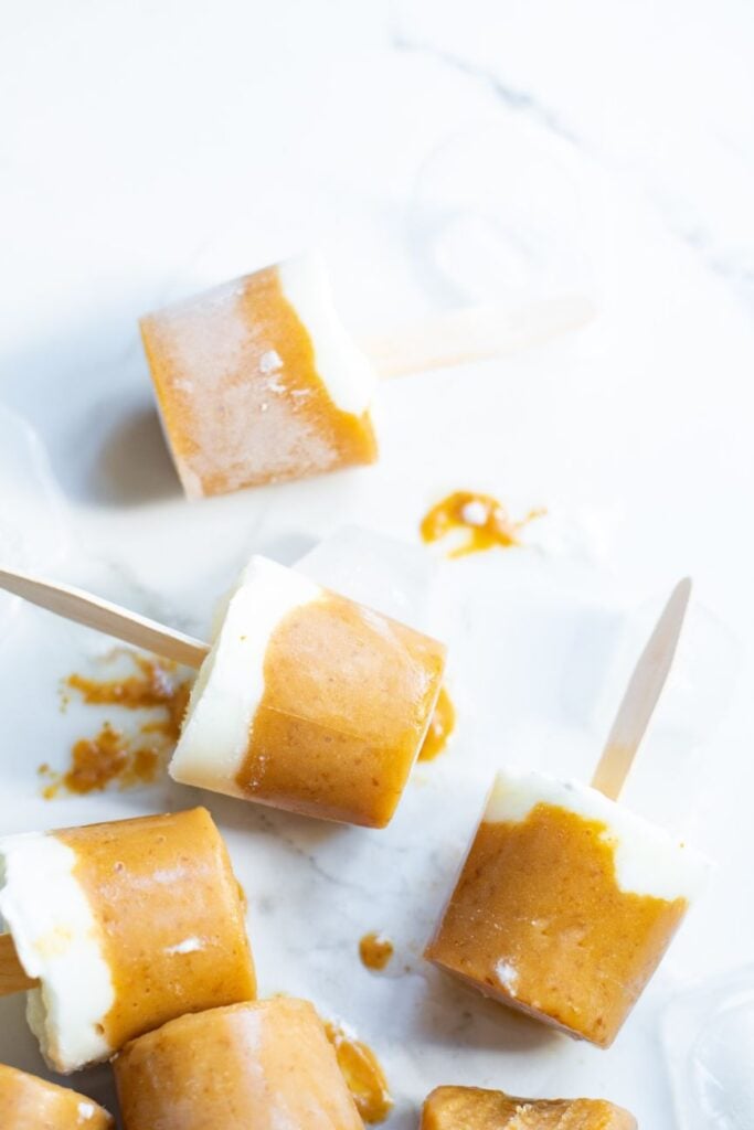 5 frozen orange and white fruit popsicles on a white background