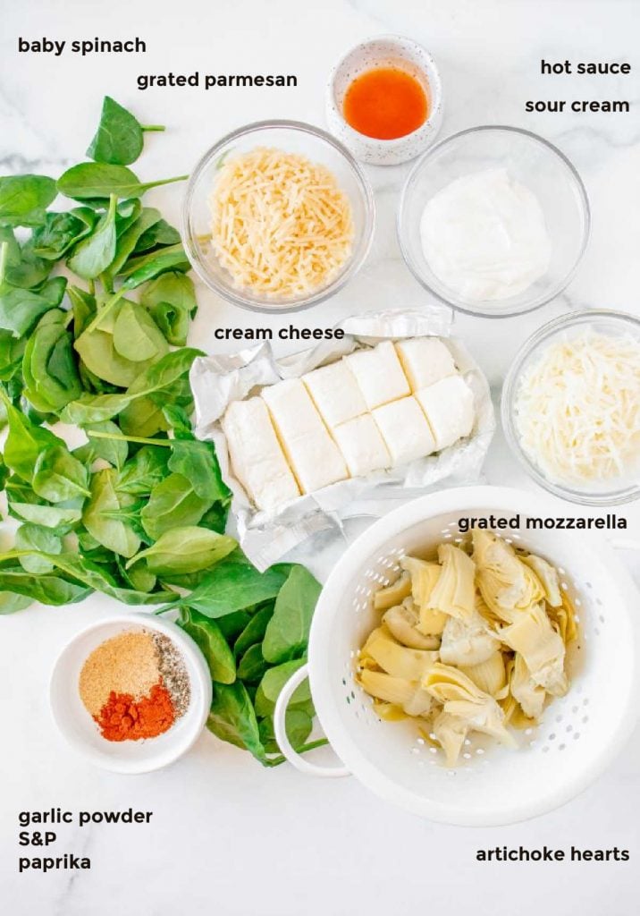 overhead ingredient shot containing baby spinach, artichoke hearts, grated cheese, spices, and sour cream