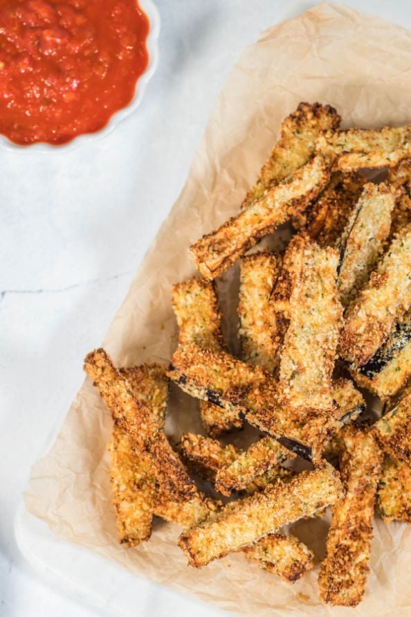 air fryer eggplant fries stacked on some parchment paper with a side of tomato sauce