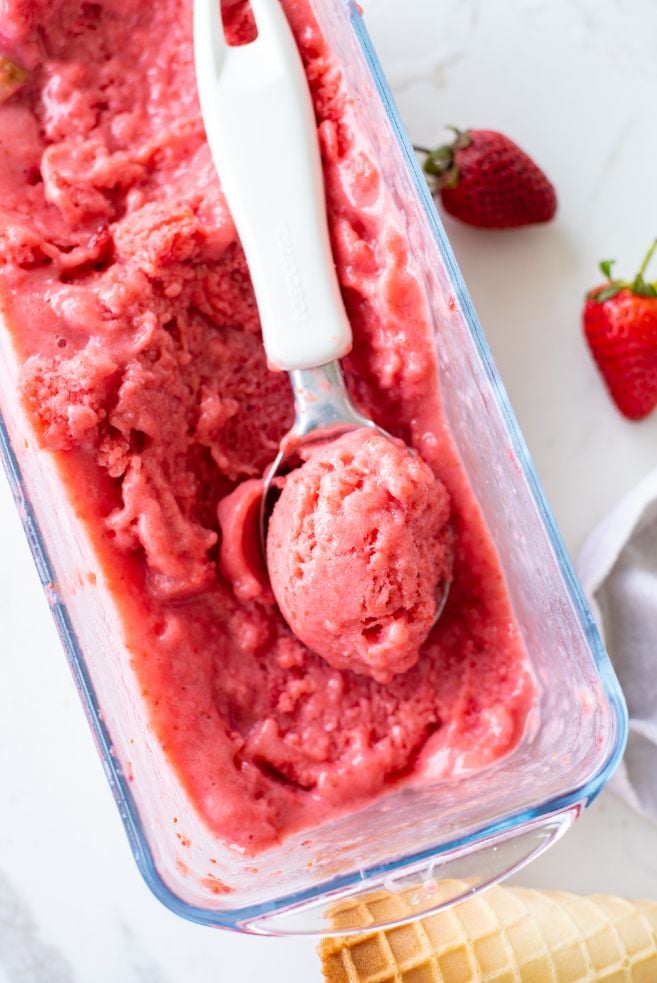 Overhead shot of strawberry ice cream in a glass container with a scoop of ice cream in an ice cream scoop