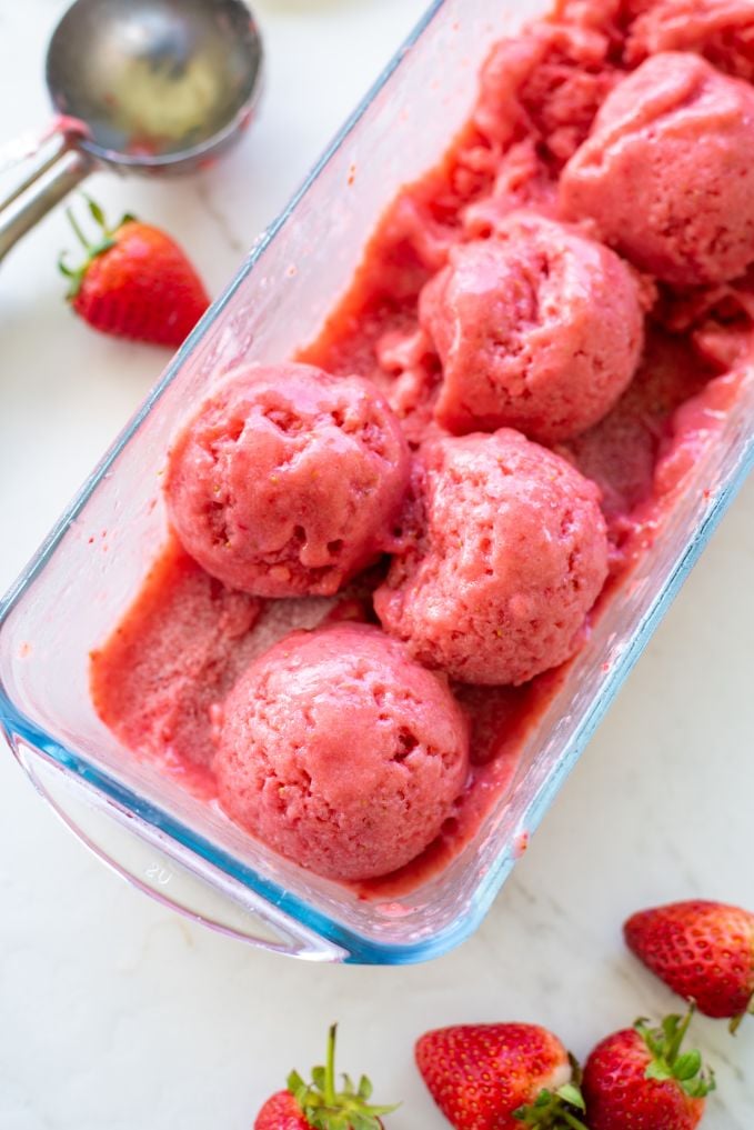 lots of scoops of strawberry sorbet in a glass ice cream container