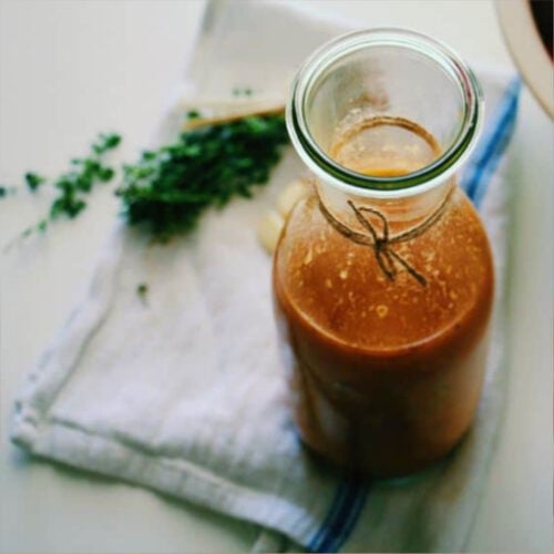 fresh tomato sauce stored in a glass jar with some fresh herbs in the background