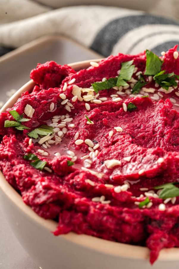 Up close shot of a bowl of beetroot hummus topped with sesame seeds and fresh parsley