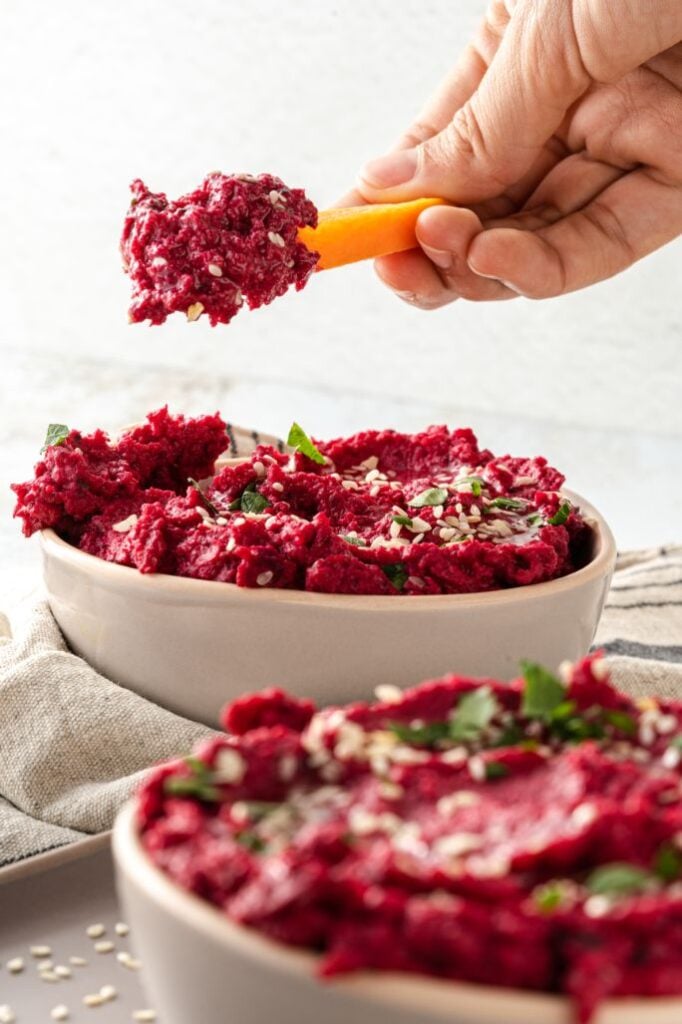 A large scoop of vegan beet dip on a carrot