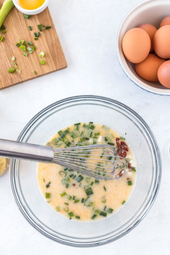 Overhead shot of eggs and green onions in a lass bowl being whisked