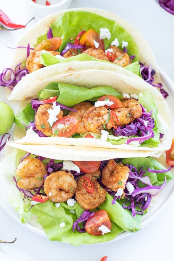 Overhead close up shot of cajun shrimp served inside tacos with lettuce, purple cabbage and cilantro