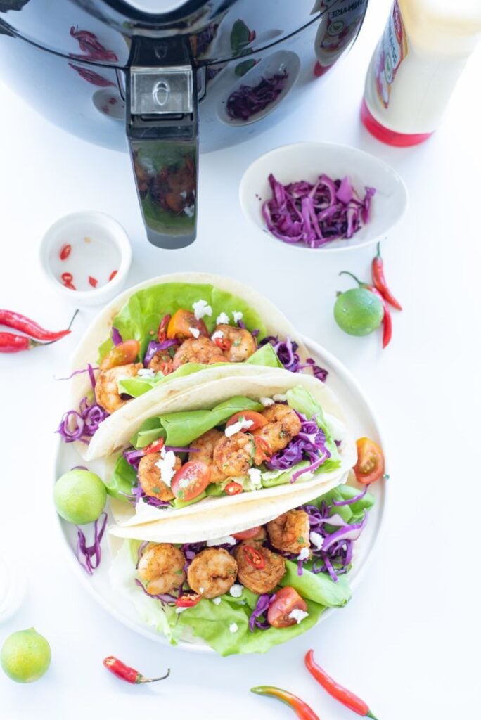 Overhead shot of shrimp tacos with an air fryer in the background