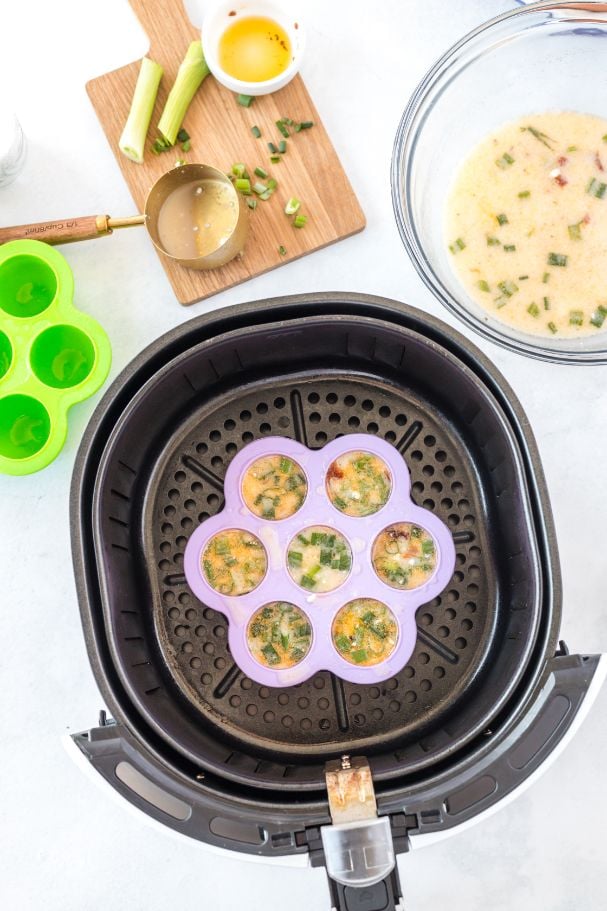 Overhead shot of a silicone mold inside the basket of an air fryer and full of raw egg and green onions