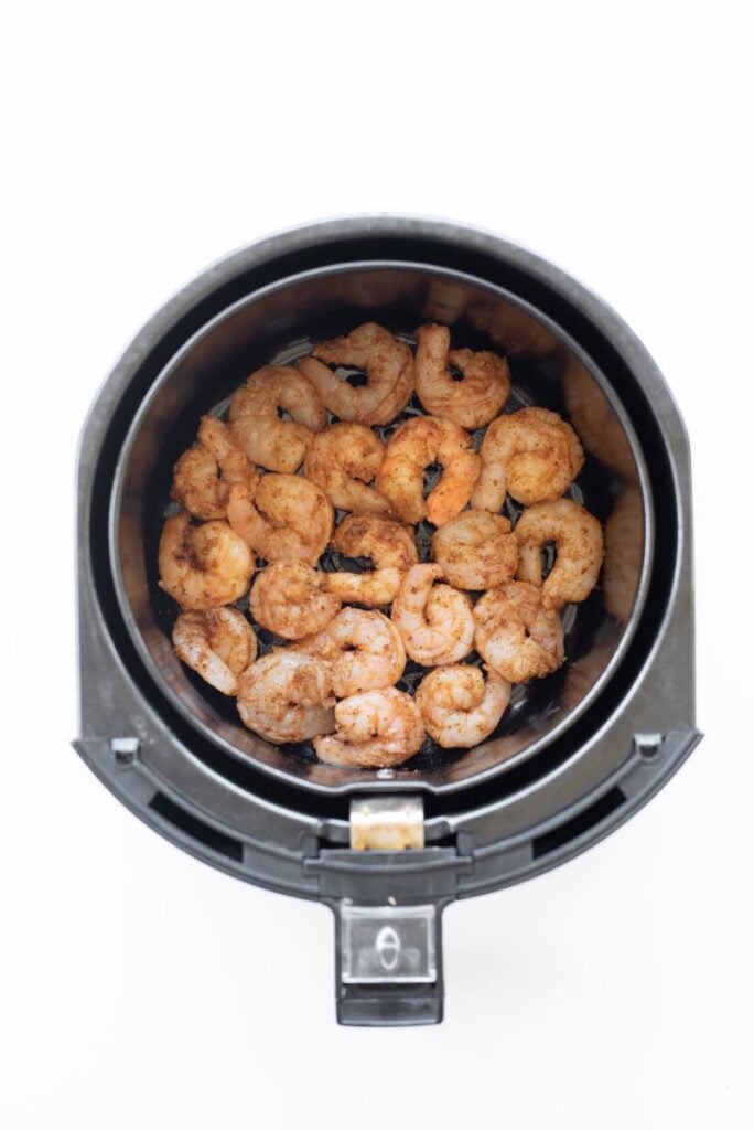 Uncooked seasoned shrimp in the basket of an air fryer in a single layer.