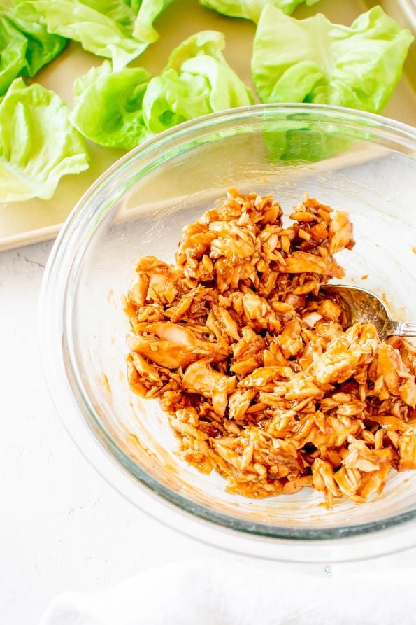 Cooked salmon mixed with a teriyaki sauce in a glass bowl. There are lettuce leaves on the side