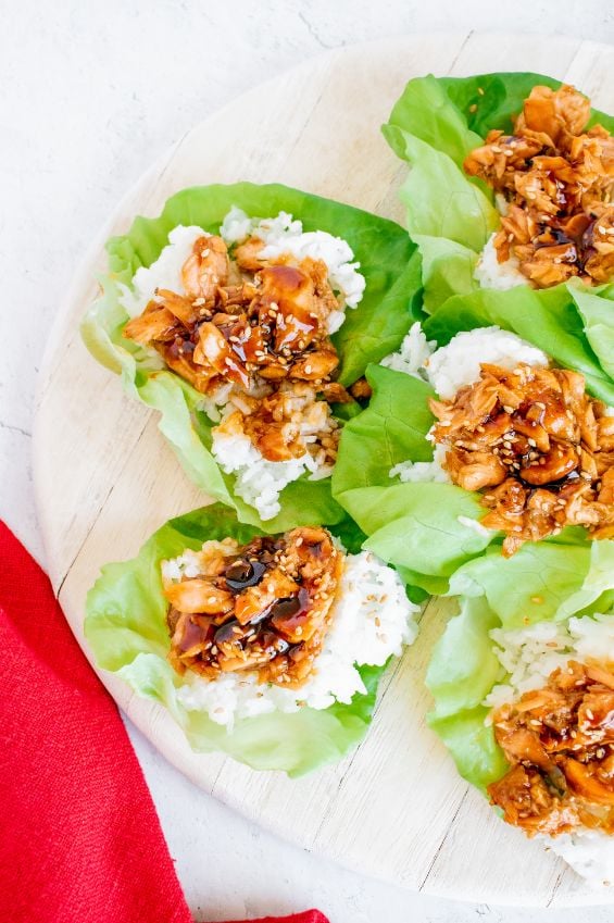 Overhead shot of salmon lettuce cups served on a wooden board with a red linen napkin on the side