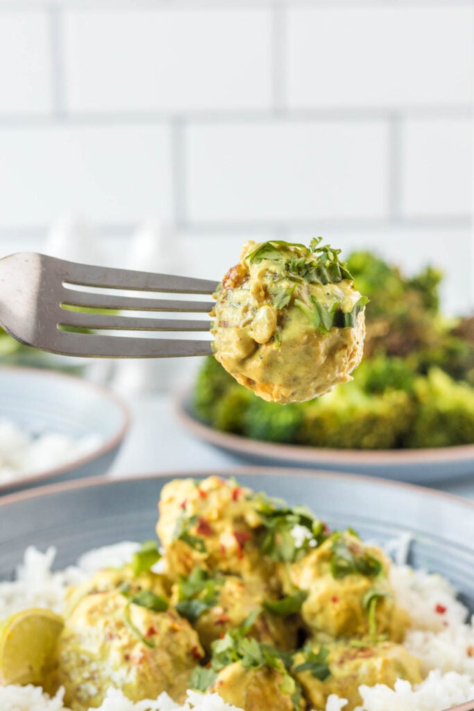 Up close shot of curry meatballs being scooped from a bowl or meatballs and rice 