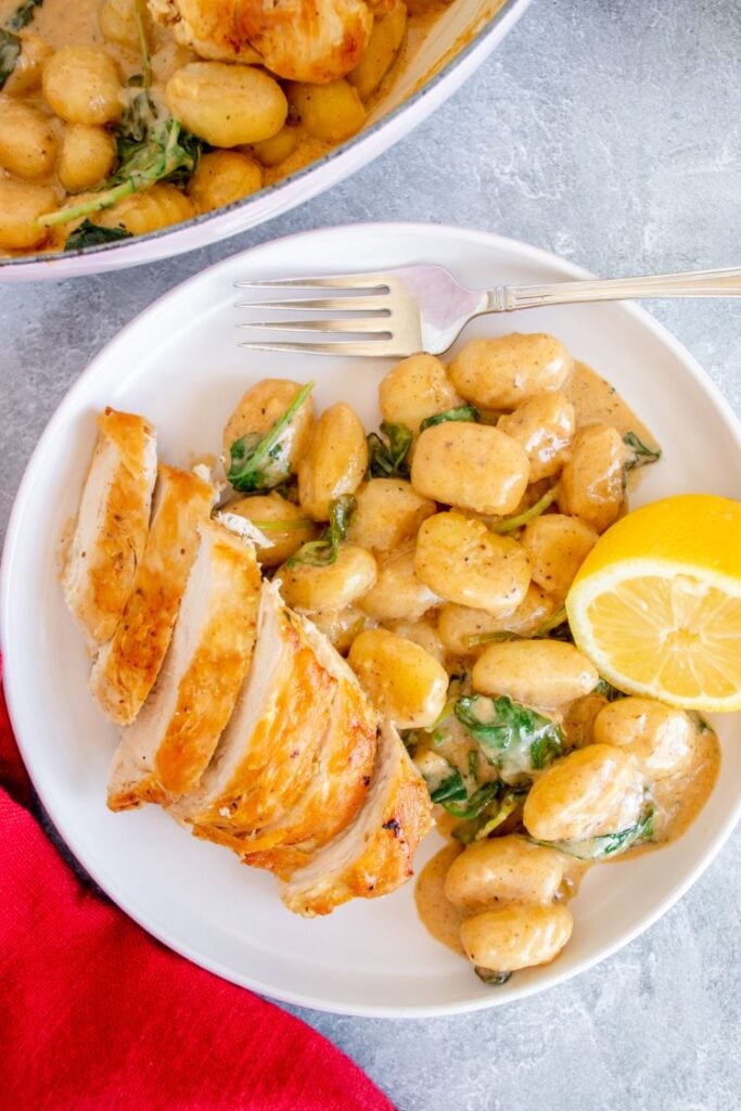 Creamy gnocchi with sliced chicken breast served on a white plate with a lemon wedge