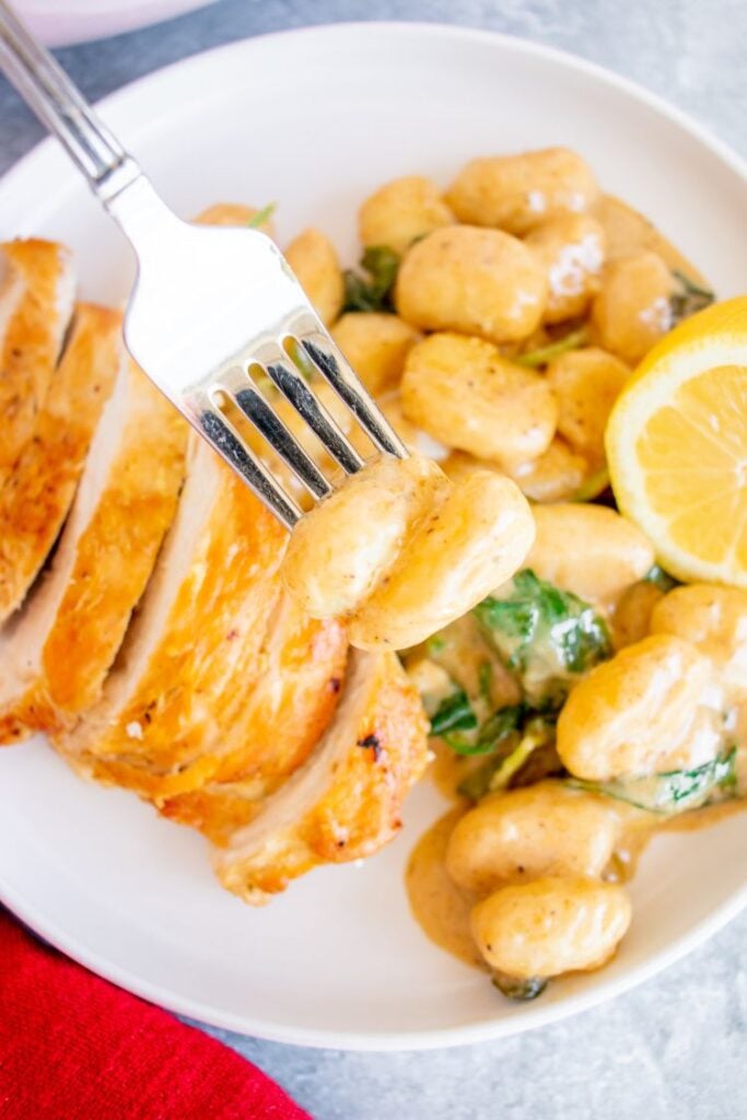 A piece of gnocchi in creamy sauce being scooped up with a fork.