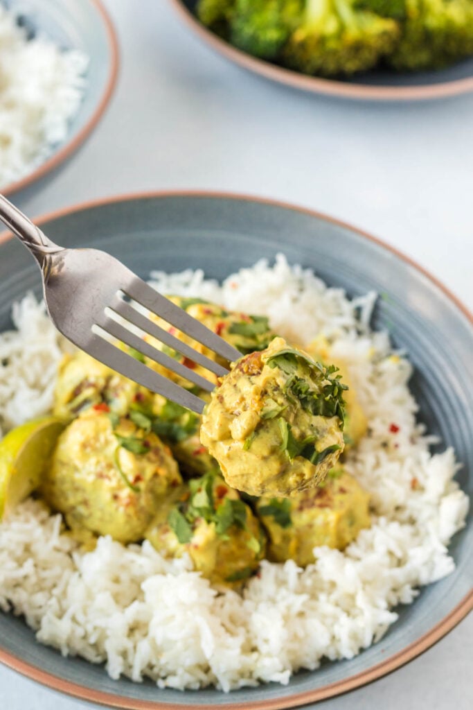 A fork scooping up a curried meatball from a bowl that also contains white rice and fresh cilantro