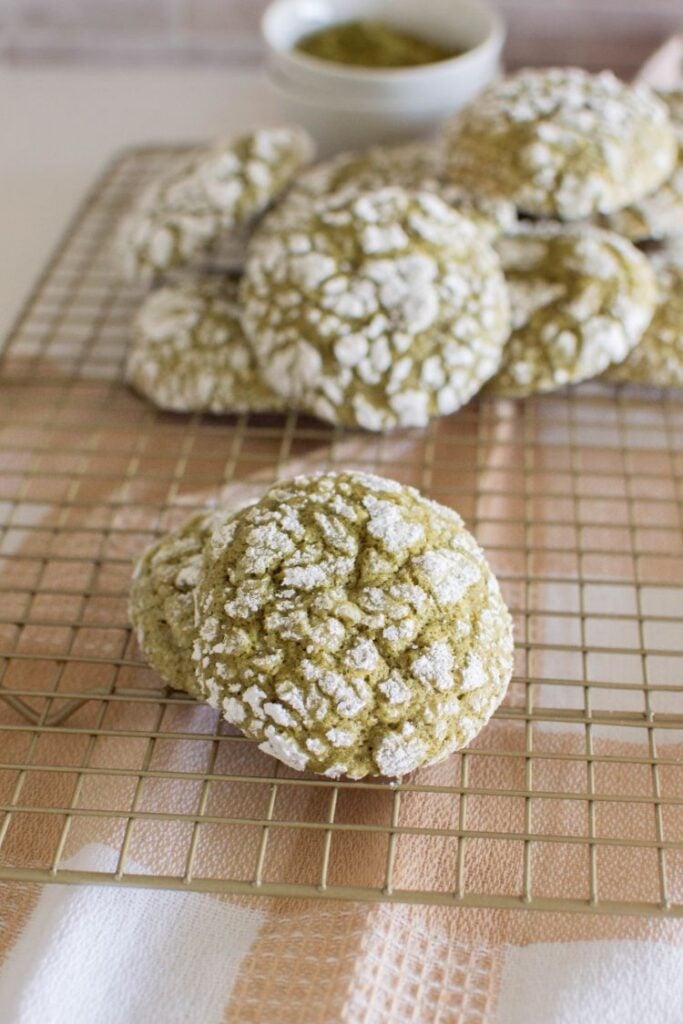 green tea cookies stacked on a wire cooling rack with a small bowl of matcha in the background.