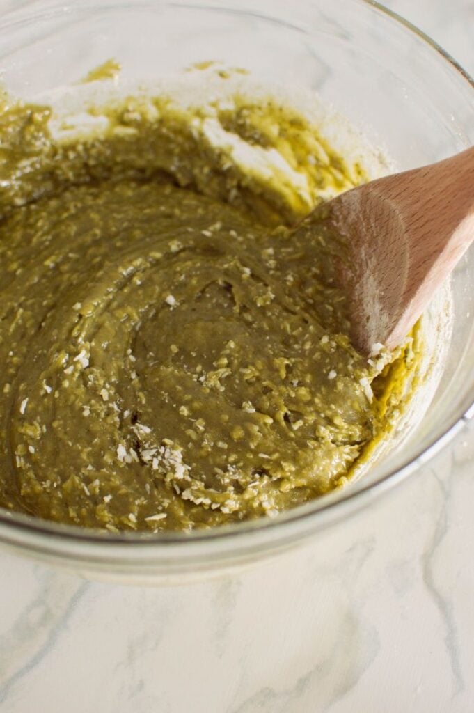 A large glass bowl containing a green batter being mixed with a wooden spoon