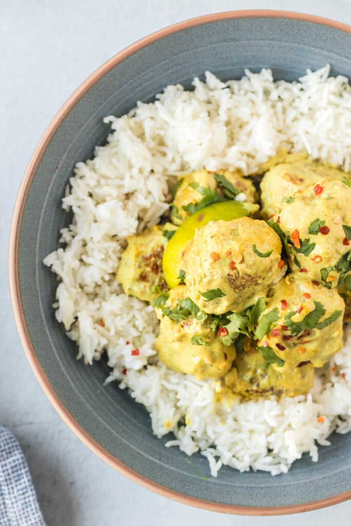 Overhead shot of meatballs served with a curry sauce and rice and topped with cilantro