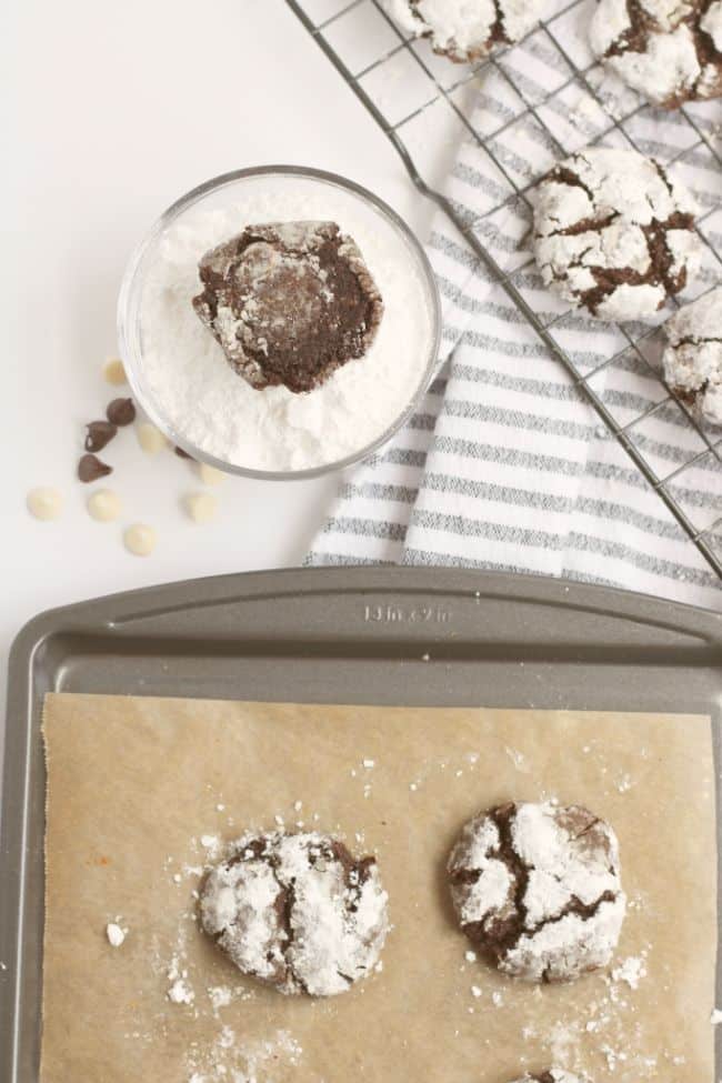 baked cookies with crinkles on top being dipped into powdered sugar and placed on a wire rack to cool
