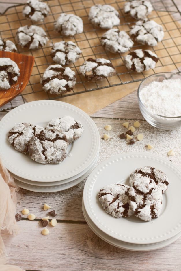 chocolate powdered cookies arranged in groups of 3 on white plates with extra cookies cooling on wire racks in the background