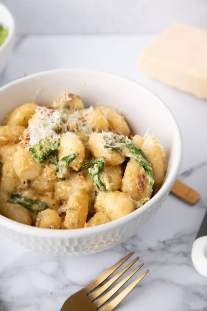 creamy spinach gnocchi served in a white bowl and topped with grated parmesan