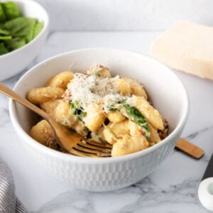 Creamy pesto gnocchi served in a white bowl with a gold fork and sprinkled with grated parmesan