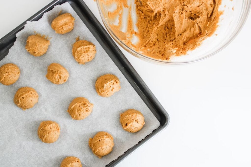 overhead shot of cookie batter being scooped onto parchment paper lined baking sheet