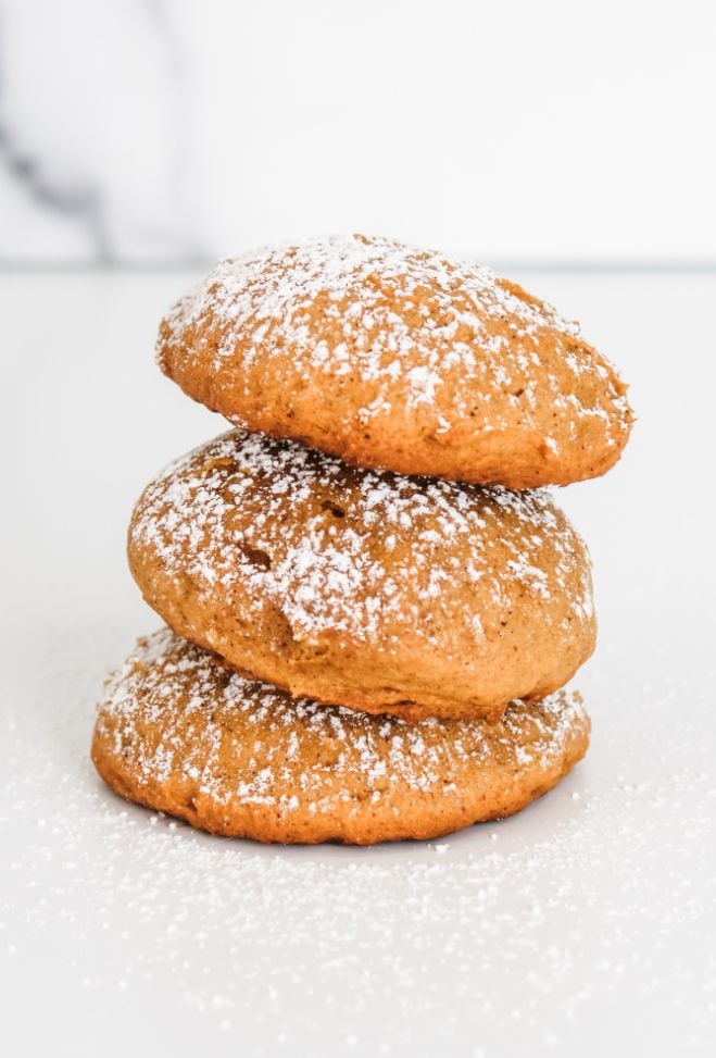 Pumpkin spice pumpkin cookies stacked three cookies tall against a white background and sprinkled with powdered sugar