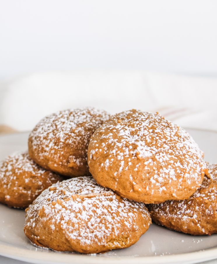 Frontal photo of some orange cookies covered in powdered sugar piled on top of each other on a white plate