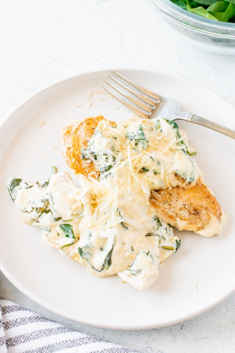 A white plate topped with chicken breasts smothered in a creamy sauce with spinach