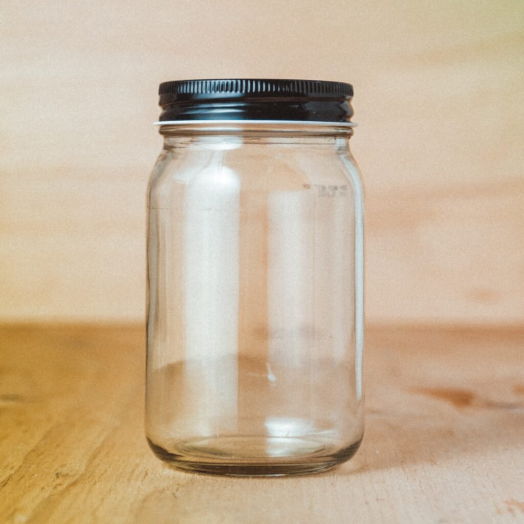 An empty mason jar sitting on a wooden bench