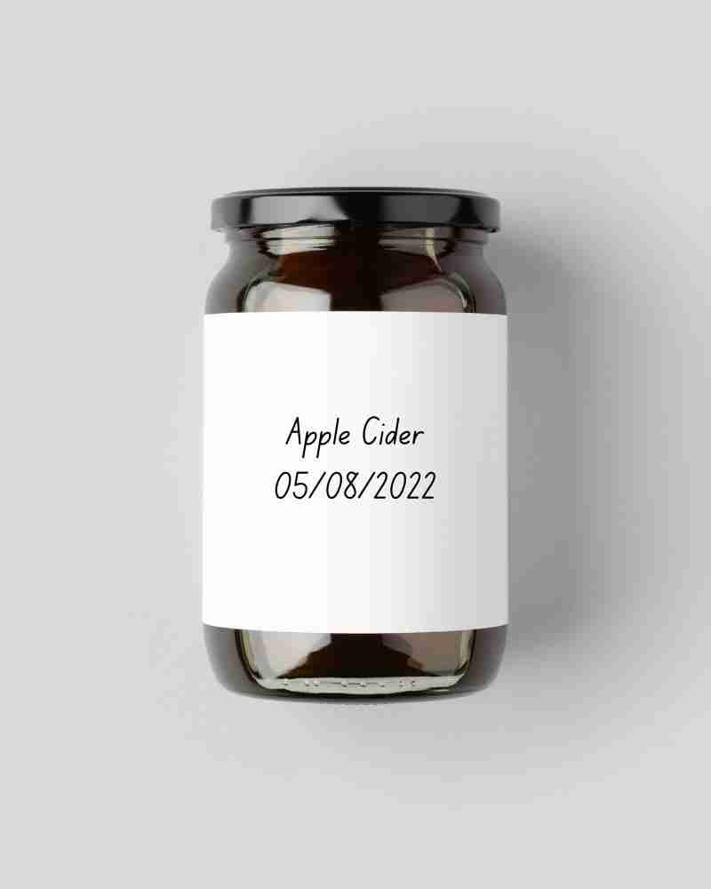 A dark glass jar with a white label saying apple cider and a date