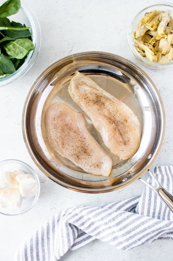 Two chicken breasts in a large skillet seasoned with salt and pepper